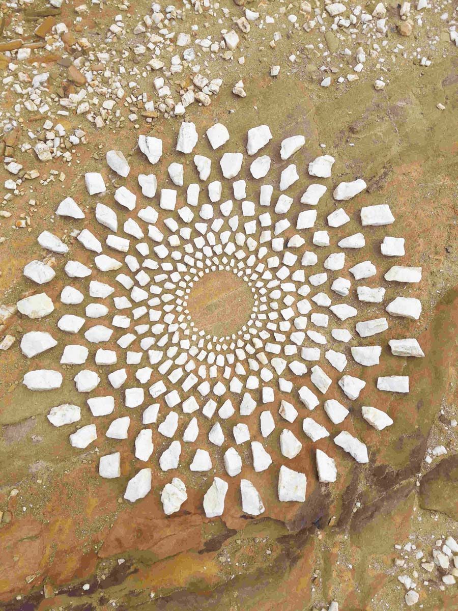 Ein aus hellen Steinen gelegtes Mandala auf rotbraunem Fels